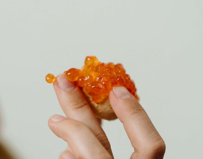 Hand holding caviar on bread, one of the foods some find unappealing despite its global popularity.