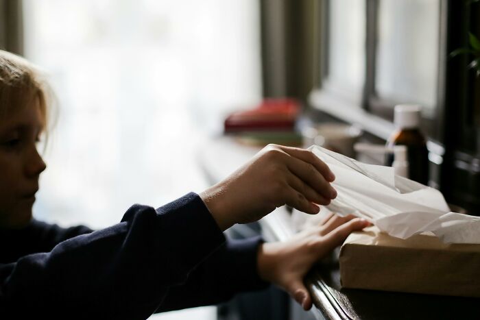 Niño sacando pañuelo de caja sobre mesa de clase media en casa, con frascos al fondo.