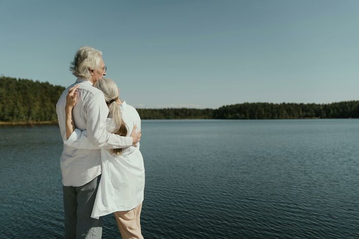 Elderly couple embraces by a serene lake, reflecting on life's regrets, linked to hospital workers' shared insights.