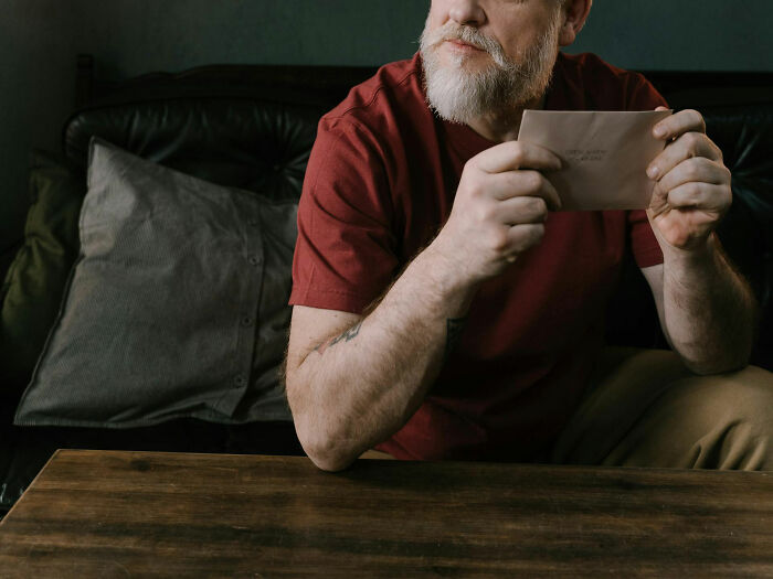 Man in a red shirt holding an envelope, contemplating an unexpected work bonus.