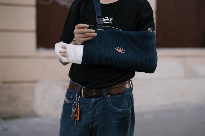 Person with an injured arm in a sling, casually dressed in jeans and a t-shirt, outdoors; unusual medical case theme.