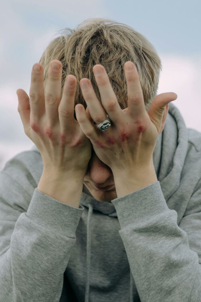 A person in a gray hoodie covers their face with hands, displaying signs of emotional distress, related to judgment by therapists.