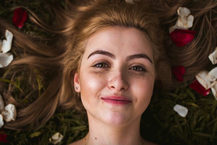 Smiling woman lying on grass with rose petals, embodying heartfelt compliments.
