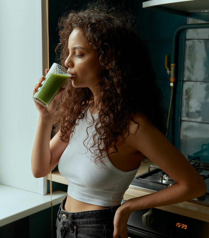 Young woman in a kitchen drinking a green smoothie, symbolizing misunderstood healthy choices.