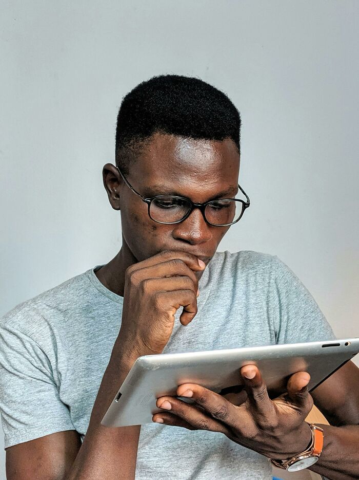 Person in glasses holding a tablet, appearing thoughtful, possibly reflecting on unprofessional things seen at work.