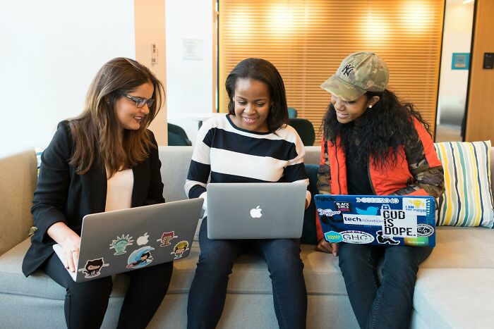 Three people sitting on a sofa, each using a laptop, discussing ideas.
