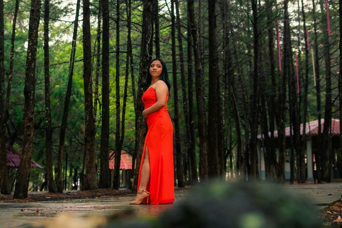 Woman in a bright red dress standing in a forest, representing unprofessional work attire in an outdoor setting.