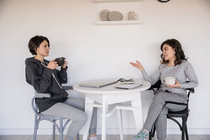 Two women in casual clothes having a serious conversation over coffee at a small table, highlighting friendship issues.
