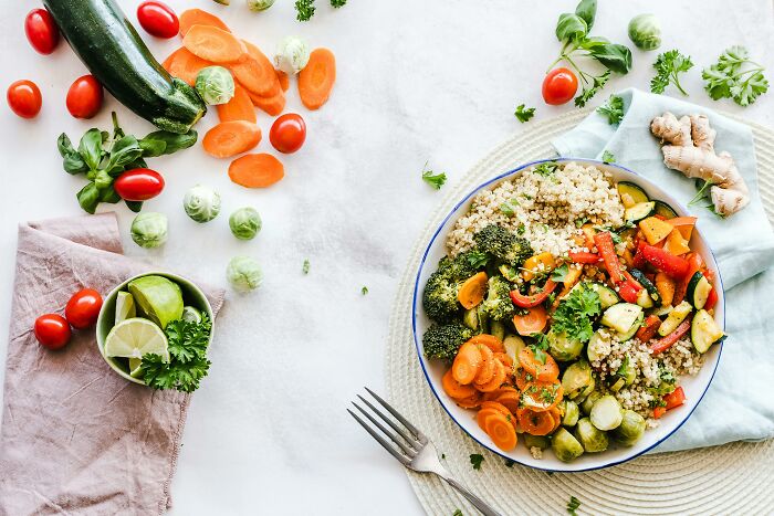 Healthy vegetable quinoa salad with carrots, broccoli, and zucchini on a table, surrounded by fresh ingredients.