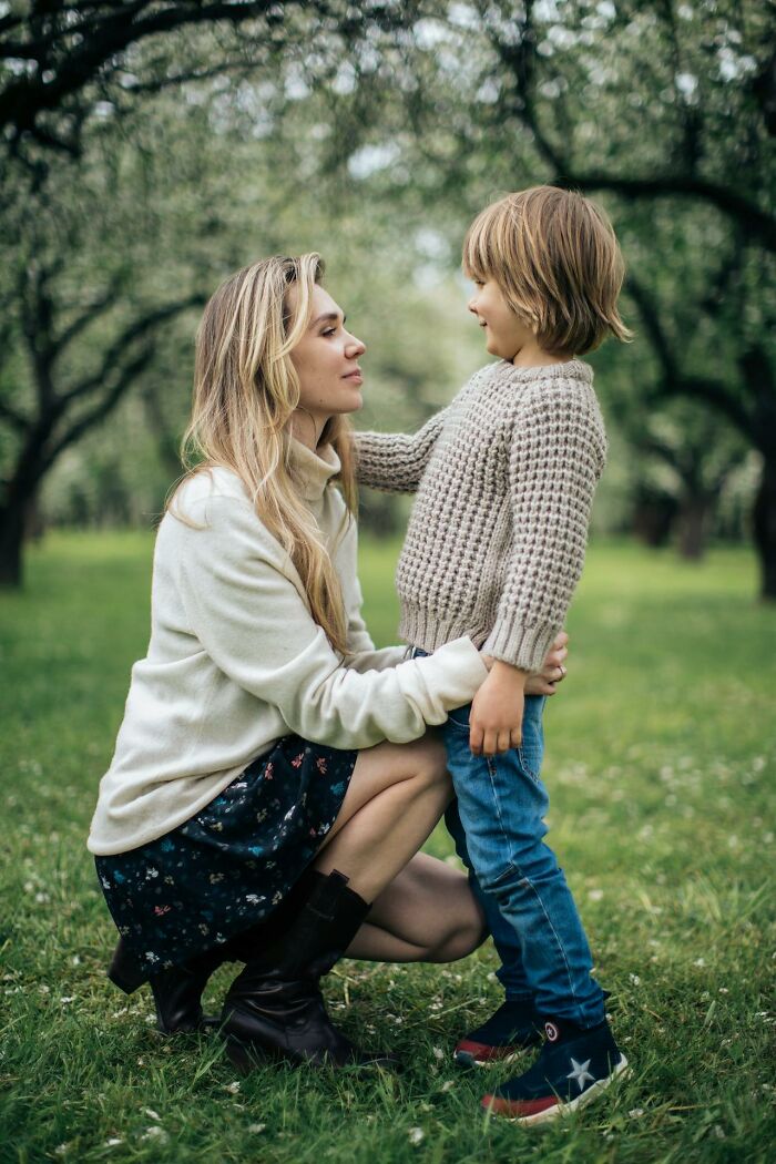 A woman kneeling and smiling at a child in a garden, highlighting judgment in therapy sessions.