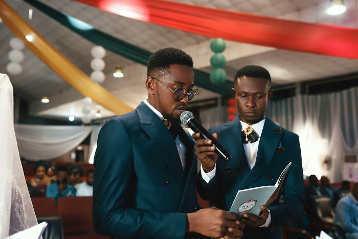 Two groomsmen in blue suits speaking at a wedding ceremony, adding a unique touch to the day.
