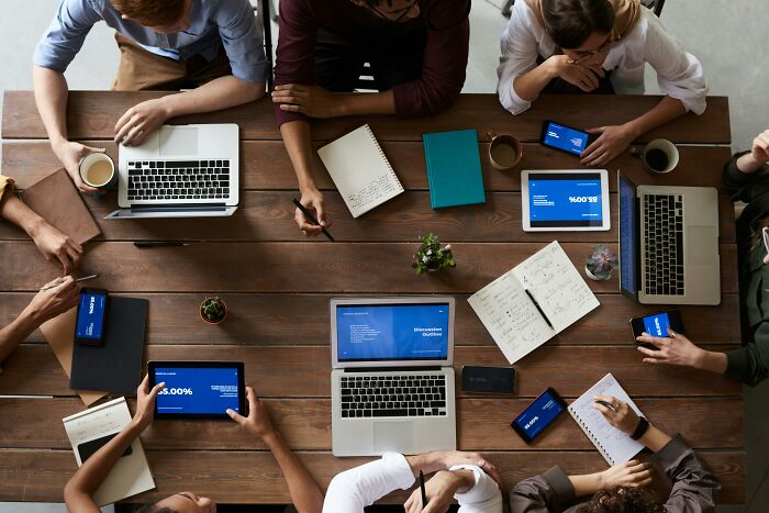 Hospital workers discussing patient regrets around a table with laptops and tablets.