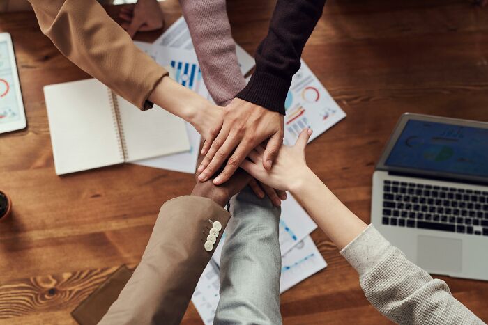 Hands joined over a desk with laptops and documents, symbolizing unity in hating overused office expressions.