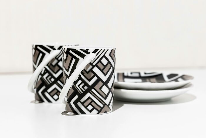 Tazas y platos con diseño geométrico modernos, típicos de clase media, sobre una mesa blanca.