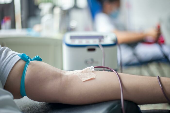 Person donating blood in a medical setting, with focus on forearm and IV needle, showcasing historical medical practices.
