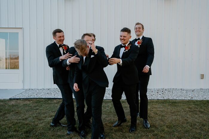 Groomsmen in black suits laughing and playfully hugging outdoors at a wedding, showcasing potential red flag behavior.