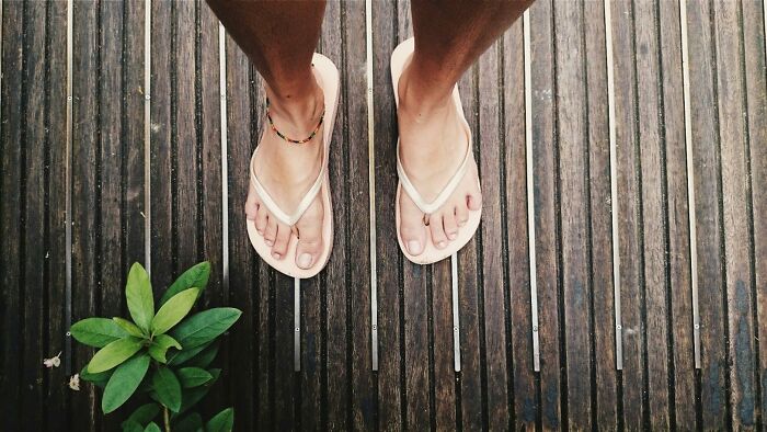 Unprofessional work attire: person wearing flip-flops on wooden deck with a plant nearby.