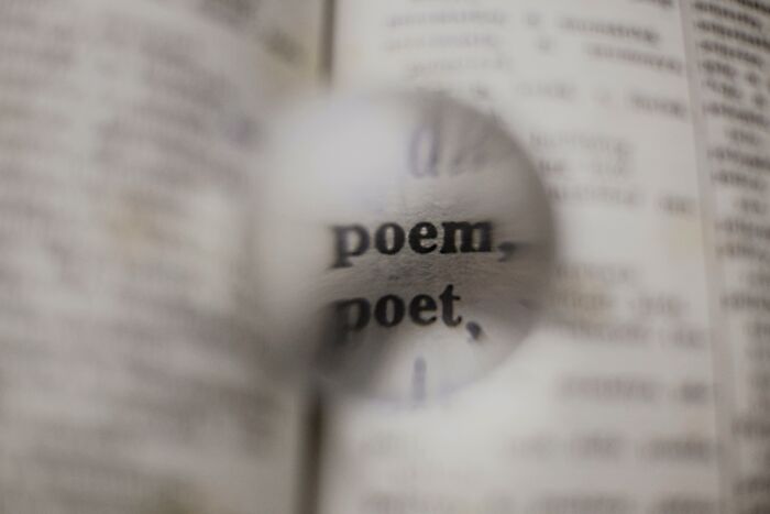 Magnifying glass focusing on the words "poem, poet" in a dictionary, highlighting world language concepts.