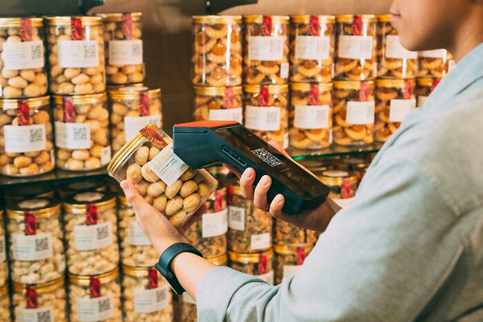 Person scanning jar of snacks in a store, questioning frugal hacks effectiveness.