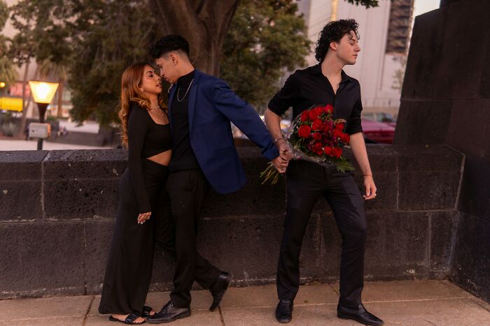 Three people in a romantic setting; one person holding roses, depicting diverse dating experiences for bisexuals.