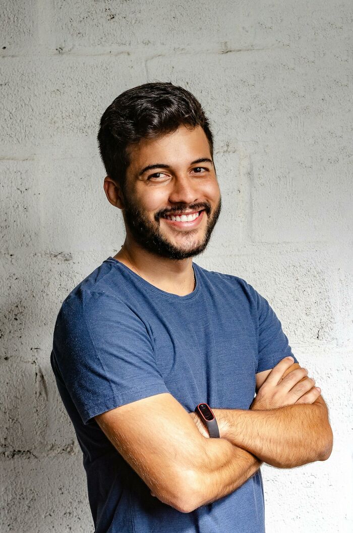 Smiling man in a blue shirt with a fitness tracker, highlighting natural beauty against a textured wall.