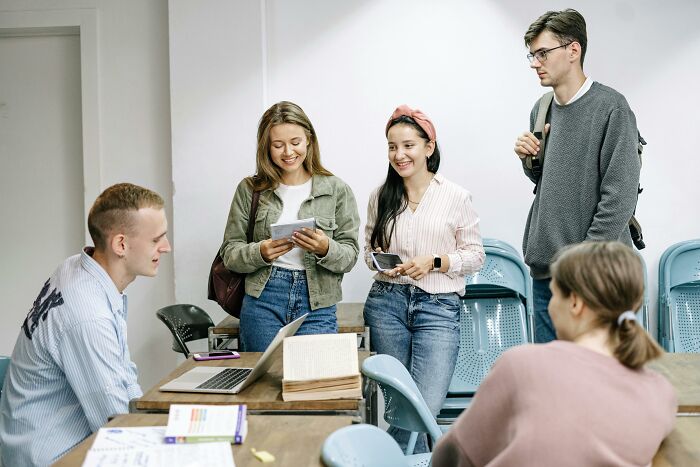 Young adults in casual clothes chatting around a classroom table, illustrating society's normal interactions.