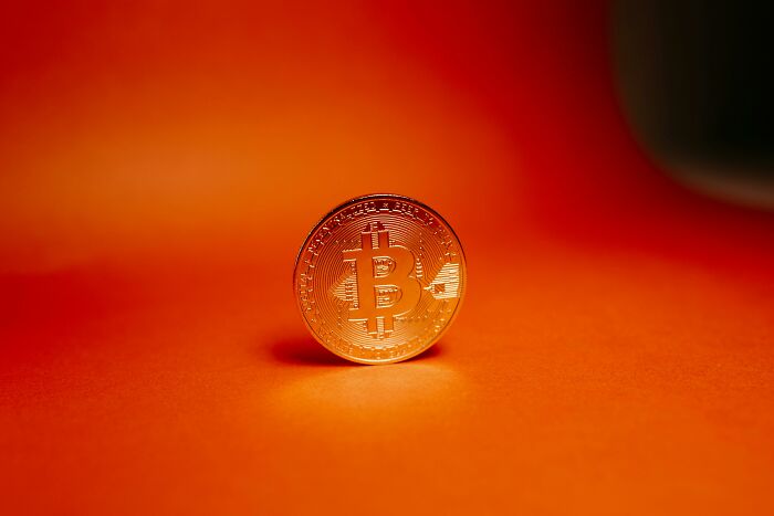 Bitcoin coin on an orange background, representing sneaky scams in cryptocurrency investments.