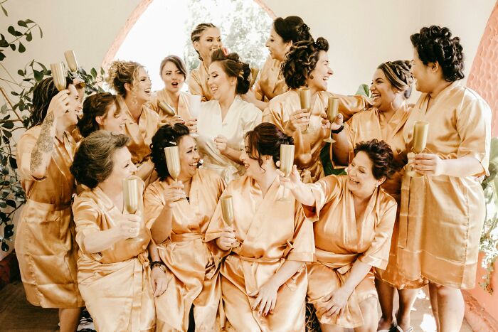 Bridesmaids in gold robes gathered with champagne, sharing laughs before the unforgettable wedding day.