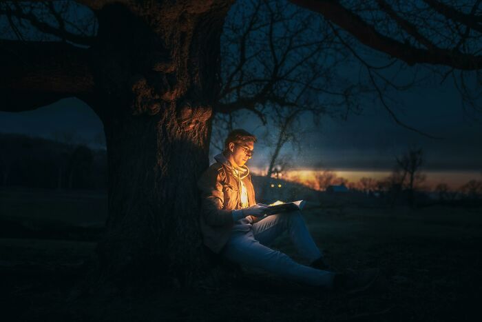 Man reading a glowing book under a tree at dusk, evoking an enchanting fairytale atmosphere. Man reading a glowing book under a tree at dusk, evoking an enchanting fairytale atmosphere.