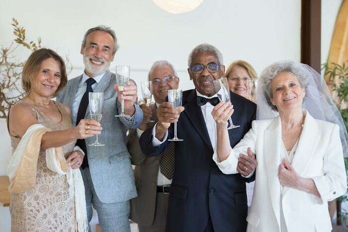 Wedding group toasting with champagne, smiling in formal attire.