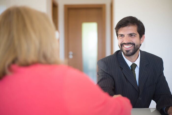 Smiling man in a suit during a challenging job interview, seated across a table.