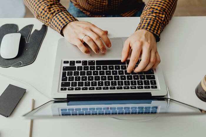 Person typing on a laptop, planning fun April Fools' pranks, with a mouse and notepad on the desk.