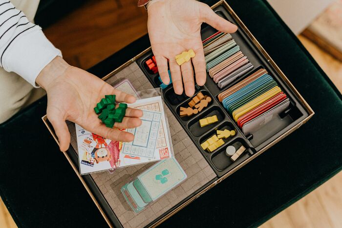Person holding board game pieces and cards, possibly illustrating tales of someone making things worse for everyone.