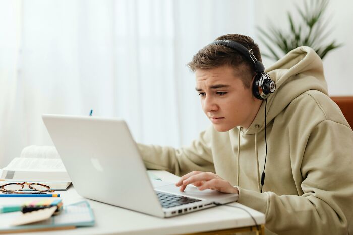 Young person in a hoodie and headphones using a laptop, focused on avoiding overused office expressions online.