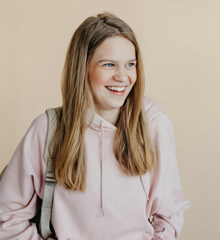 Smiling woman in a pink hoodie, looking to the side, against a plain background.
