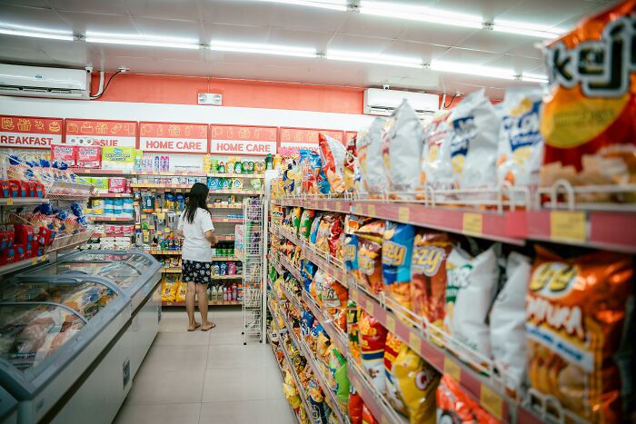 Person browsing a grocery store aisle, surrounded by various snack options, contemplating frugal hacks like making bread.