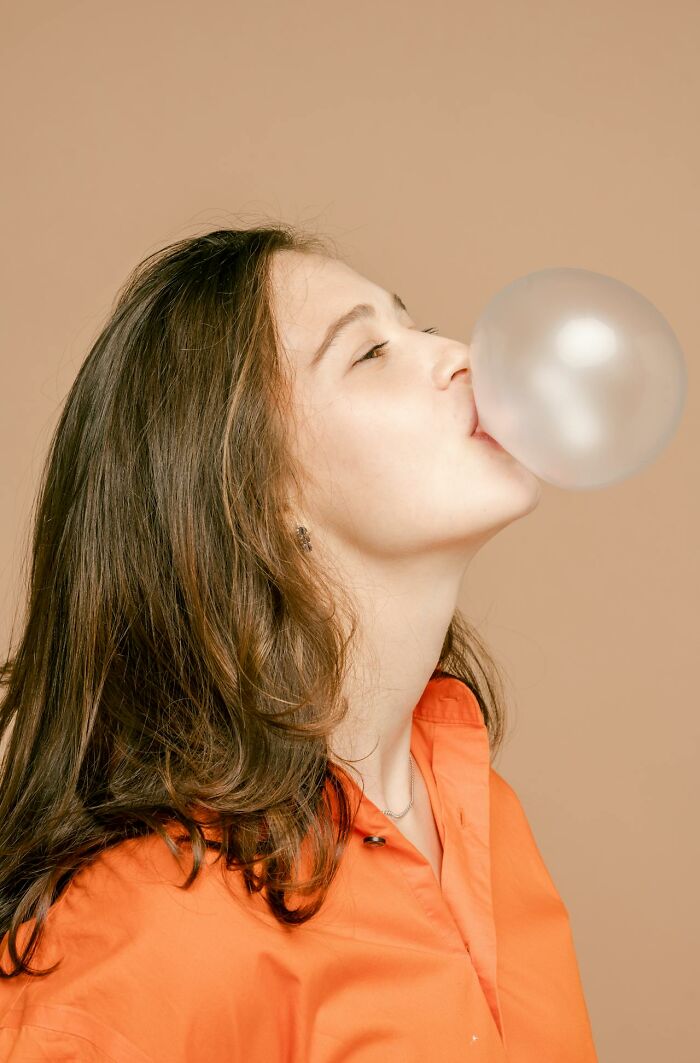 Woman in an orange shirt blowing a bubblegum bubble, showcasing a playful moment related to an eating competition.