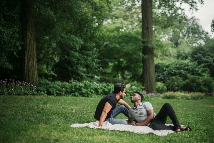 Two men sitting on a blanket in a park, enjoying a date.