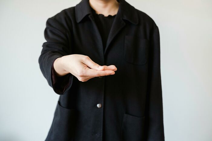 A person in a black coat extending an open palm, symbolizing rejection akin to being picked last in gym class.