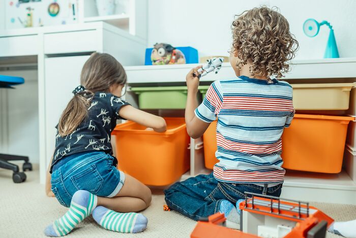 Niños jugando en una habitación con juguetes y cajas de almacenamiento, representando un hogar de clase media.