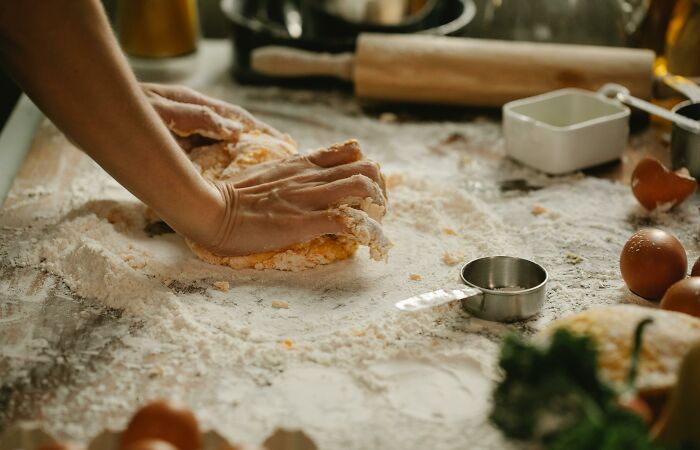 Hands kneading dough on a floured surface, with measuring cups and eggs around, illustrating homemade bread efforts.