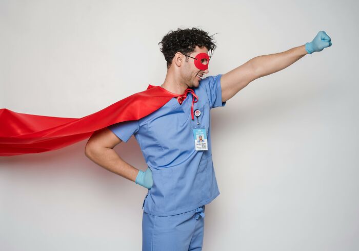 Man dressed as a superhero in scrubs, challenging common stereotypes with a playful pose.