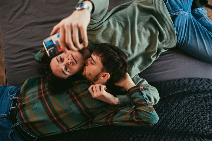A couple lying on a bed, taking a selfie, capturing moments of dating different genders.
