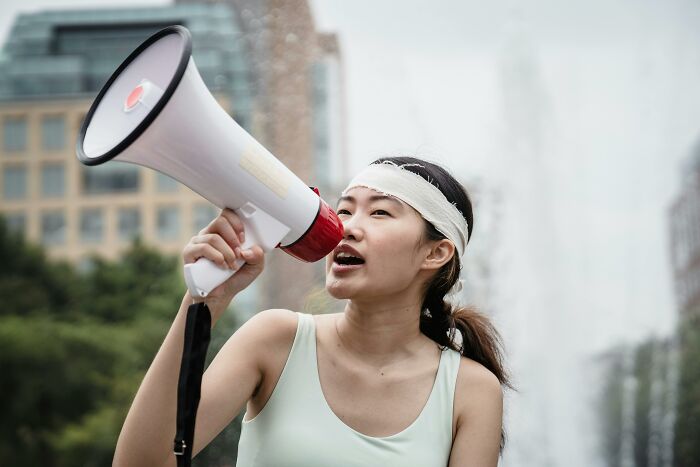 Woman shouting through megaphone, highlighting misconceptions in a city park setting.