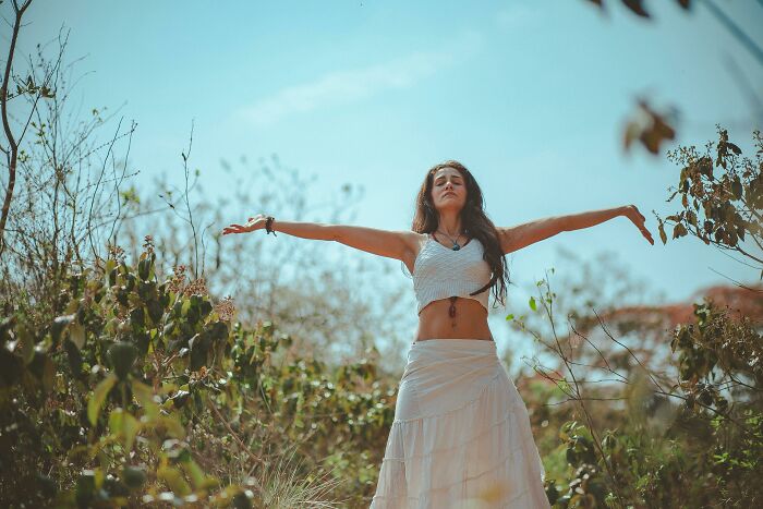 Woman in white clothing with arms outstretched in a natural setting, emphasizing serenity amidst potential scams.