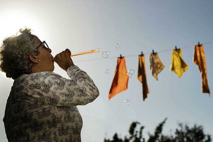 A person blowing bubbles outdoors with colorful cloths hanging, challenging common stereotypes.