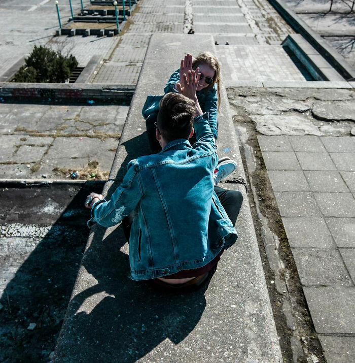 Man in denim jacket sitting outdoors, playfully interacting with a woman, capturing a moment of rejection.