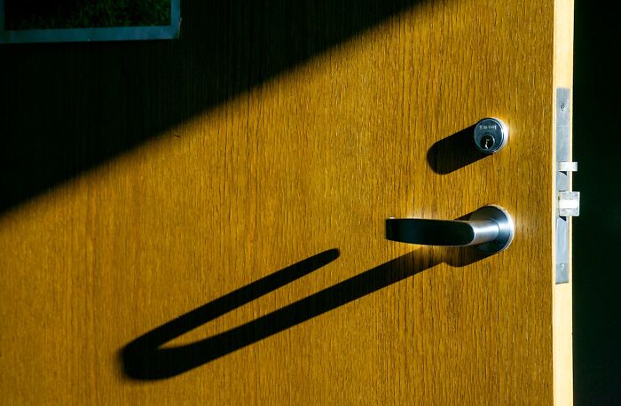 Wooden door slightly ajar with sunlight casting a shadow, creating a mysterious atmosphere.