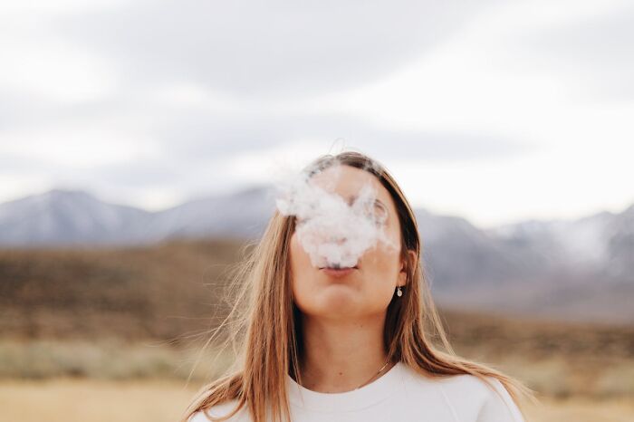 Woman outdoors with smoke obscuring her face, mountains in the background.