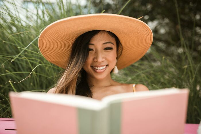 A woman with a hat smiling while reading, enjoying simple approaches for a better life outdoors.